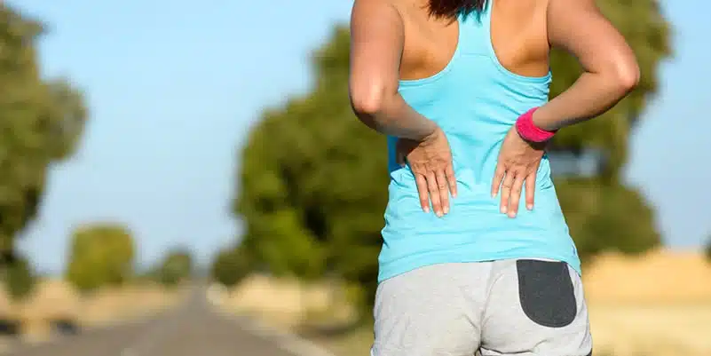 Back Pain - lady in grey shorts and blue t-shirt holding lower back