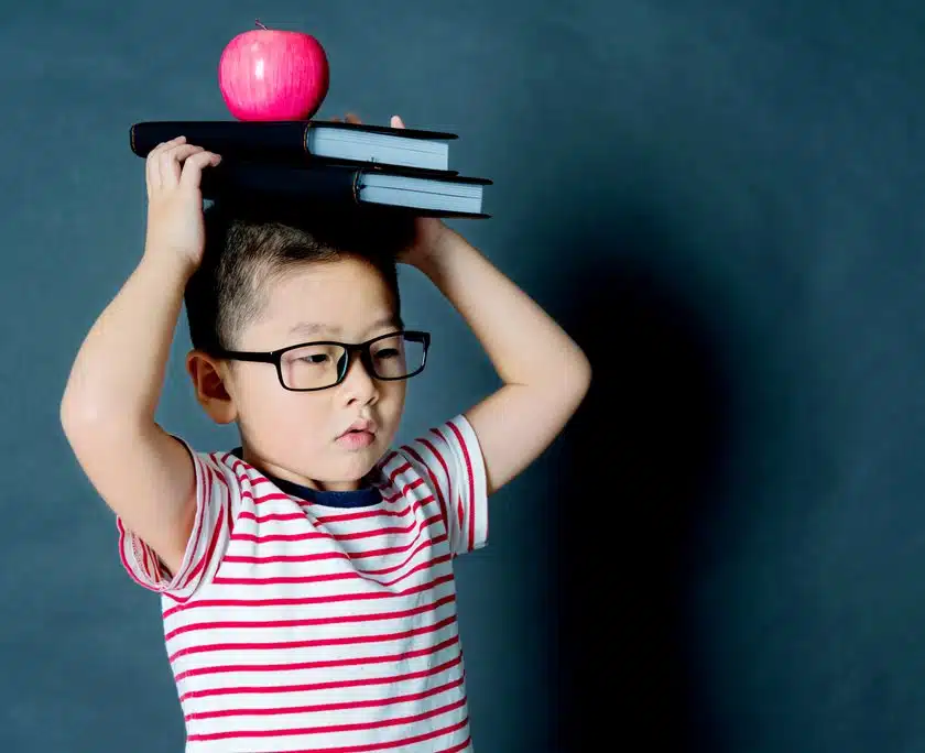 Child balancing books on his head with a pink apple Willow Chiropractic
