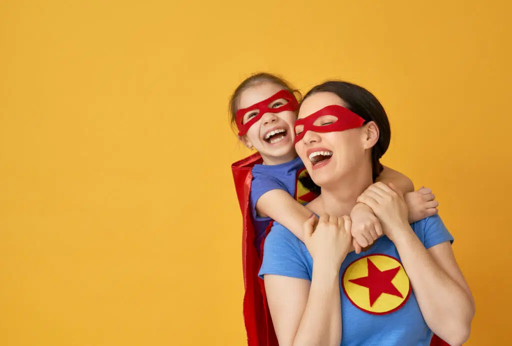 Mother and her child playing together. Girl and mom in Superhero costumes. Mum and kid having fun and smiling. Family holiday and togetherness.
